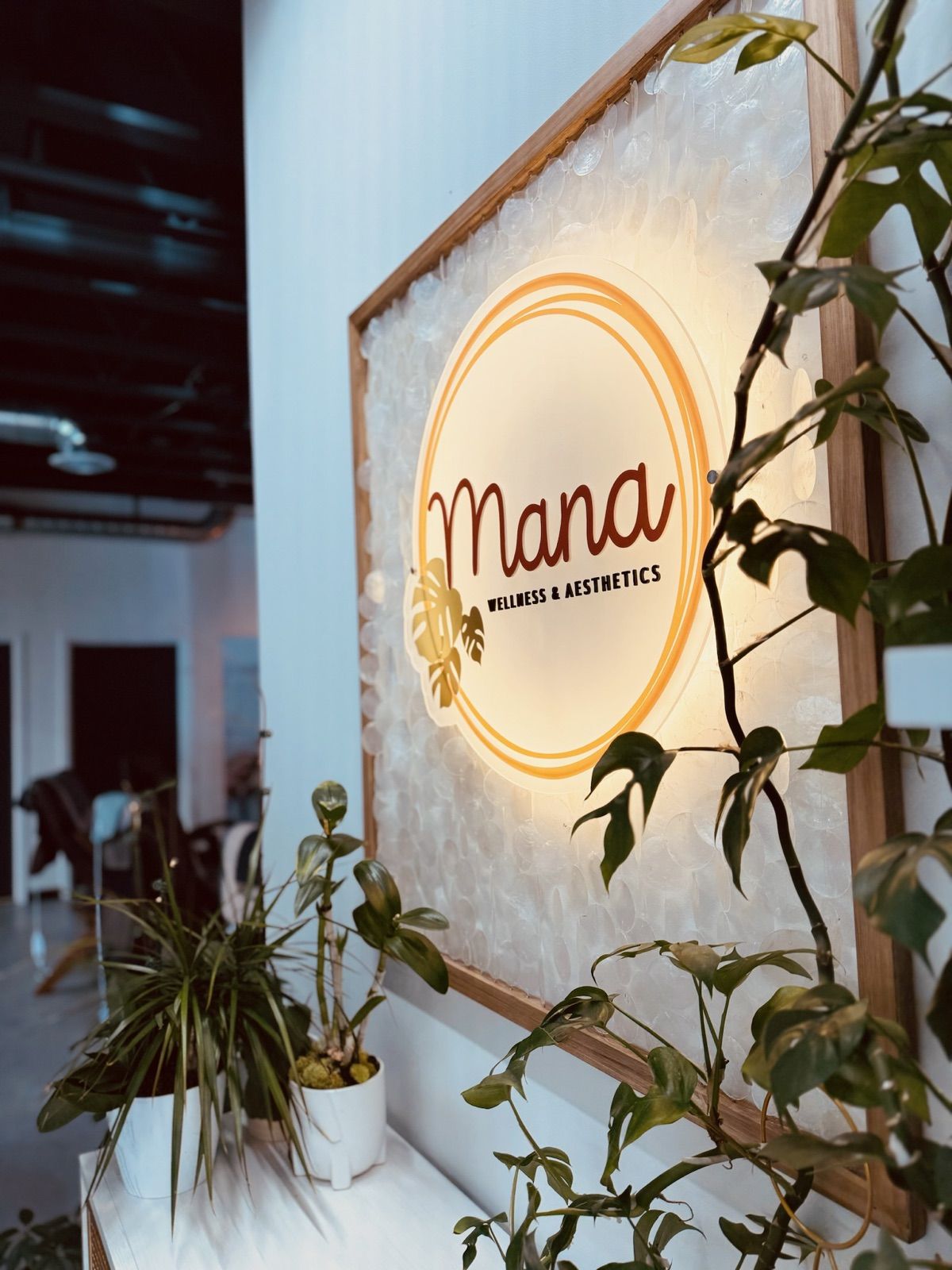 The gold Mana Wellness sign surrounded by plants